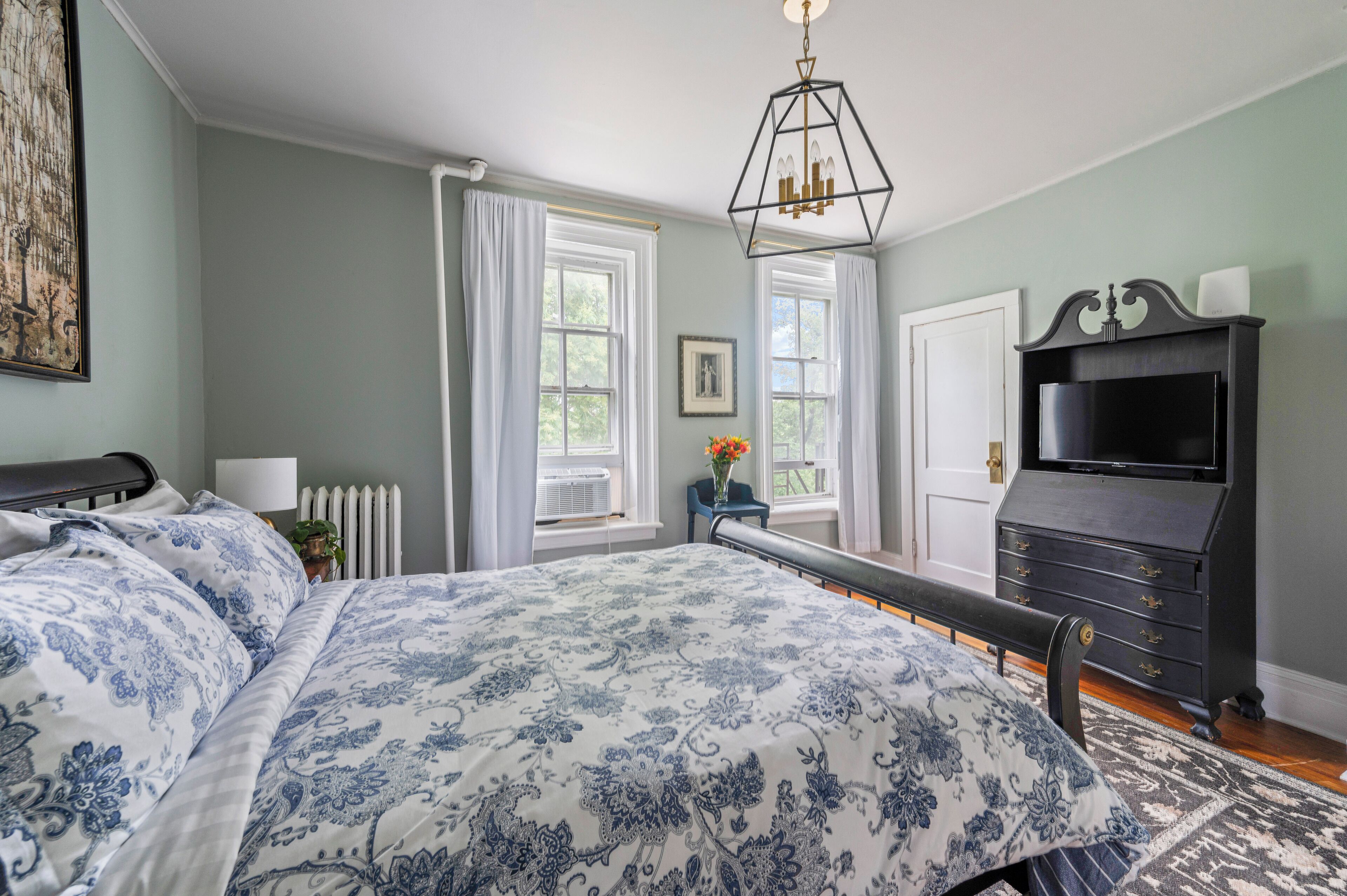 A bedroom with a large bed, a dresser, a radiator, and a window with curtains.