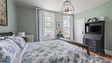 A bedroom with a large bed, a dresser, a radiator, and a window with curtains.