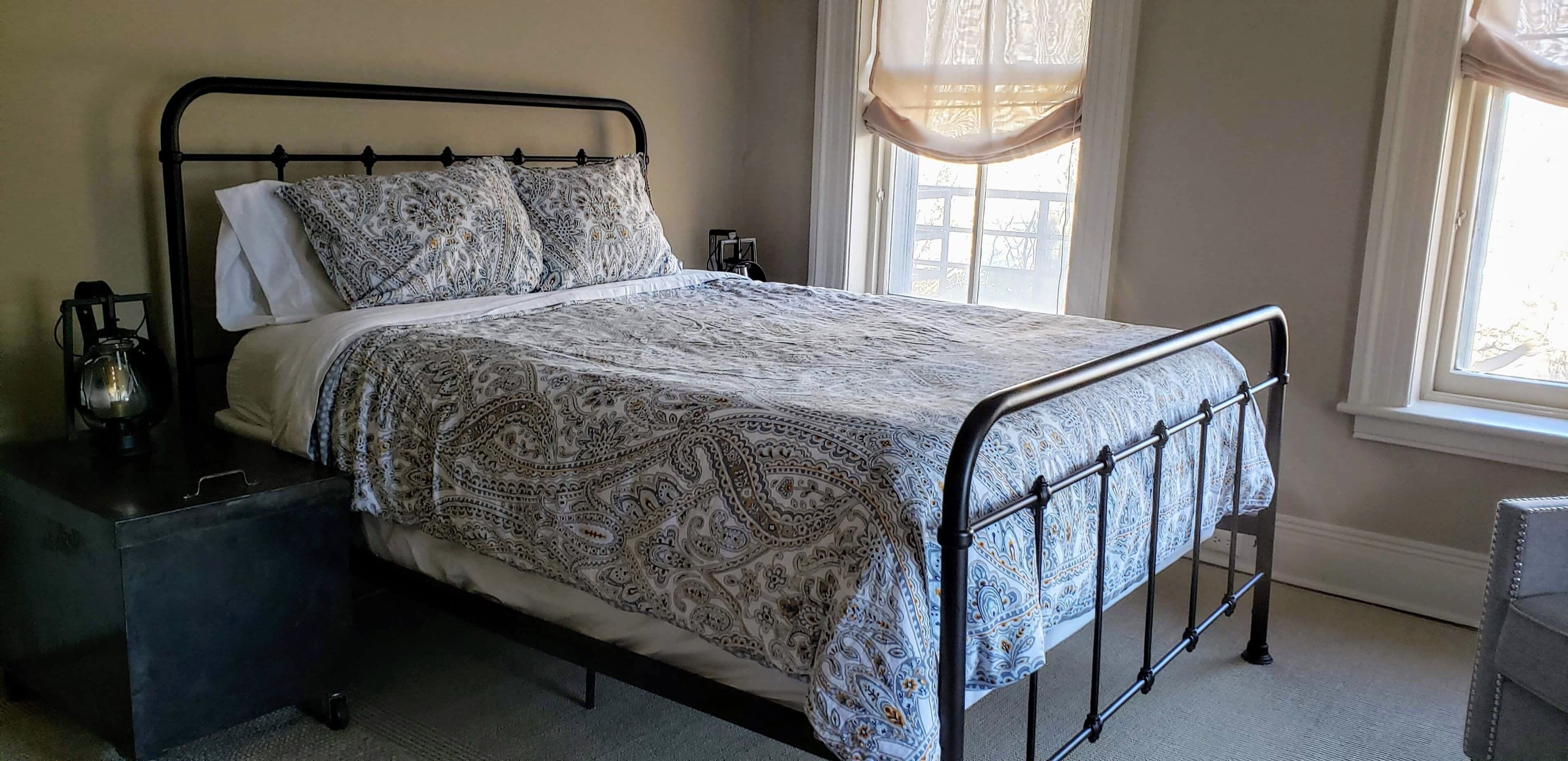A neatly made bed with a patterned bedspread, a bedside table with a lamp, and a window with curtains.