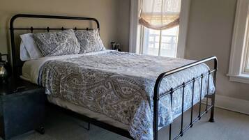 A neatly made bed with a patterned bedspread, a bedside table with a lamp, and a window with curtains.