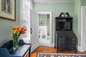 A room with a wooden floor, a black dresser, a TV, a vase with flowers, and a framed picture on the wall.