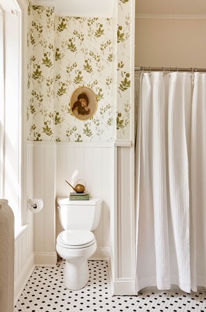 A bathroom with a toilet, a shower curtain, and a wall with floral wallpaper.