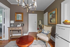 A living room with a wooden coffee table, a sofa, a white refrigerator, and a painting on the wall.