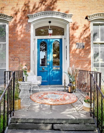 A blue door with a white frame, a small table with a chair, a rug, and potted plants on the porch.