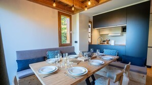A dining area with a wooden table set for six, a built-in bench with cushions, and a kitchen area with a stove and sink. - Hauts de Chantemouche 17 (Les Allues)
