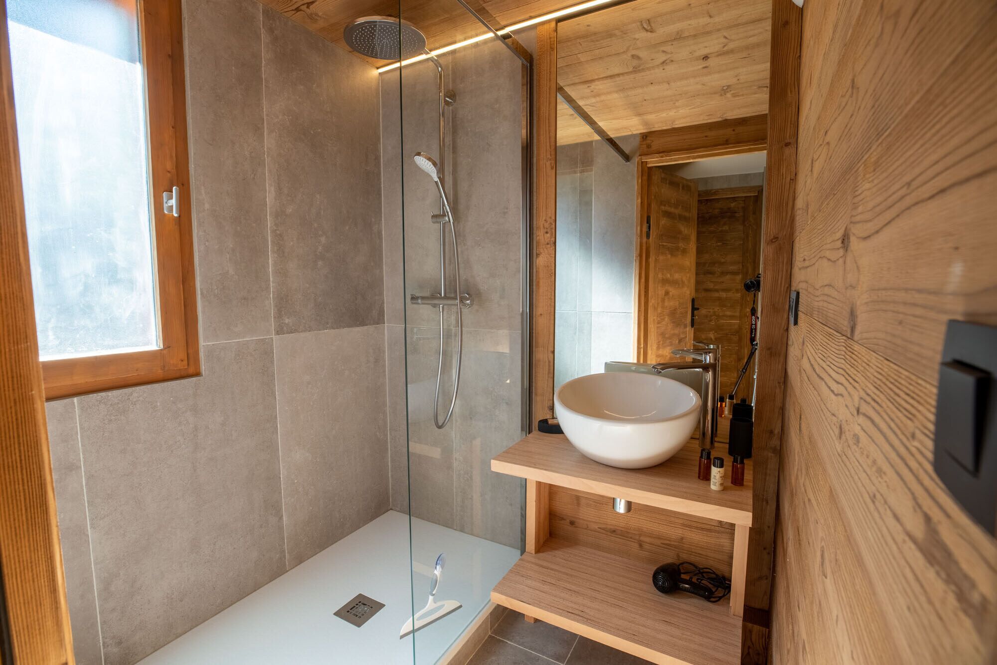 Un baño moderno con cabina de ducha de vidrio, tocador de madera con lavamanos grande y techo de madera.