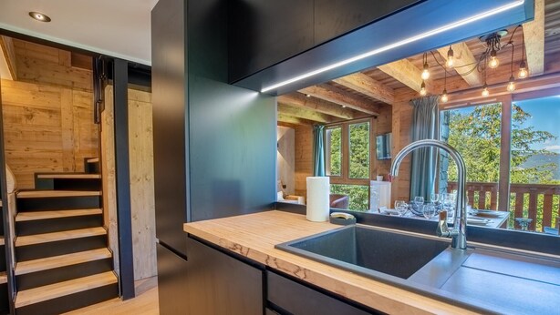 A modern kitchen with a wooden staircase, a large window with a view, and a built-in sink. - Hauts de Chantemouche 17 (Les Allues)
