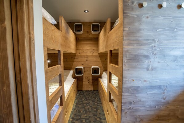 Un estrecho pasillo de madera con literas a ambos lados, que conduce a una habitación pequeña con suelo estampado.