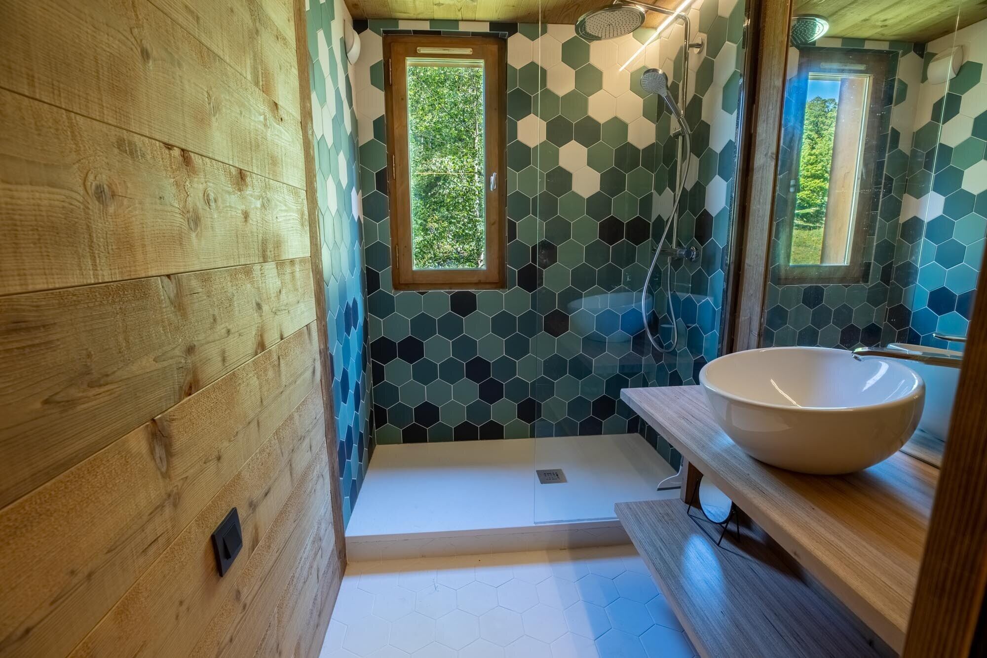 Une salle de bain avec des murs en bois, une grande fenêtre et un pare-chocs en carreaux hexagonaux.