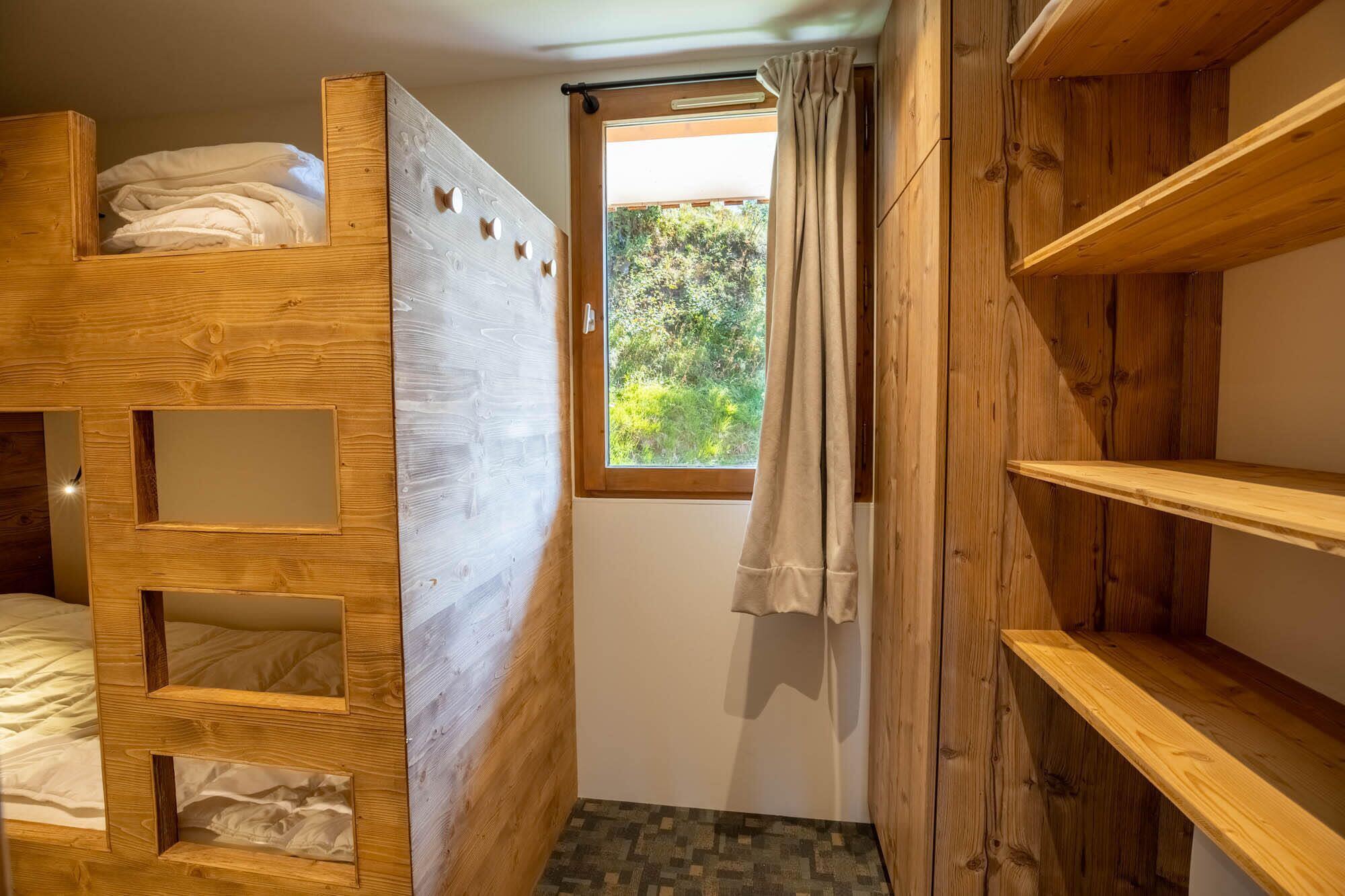 A wooden bunk bed room with a window and a curtain.