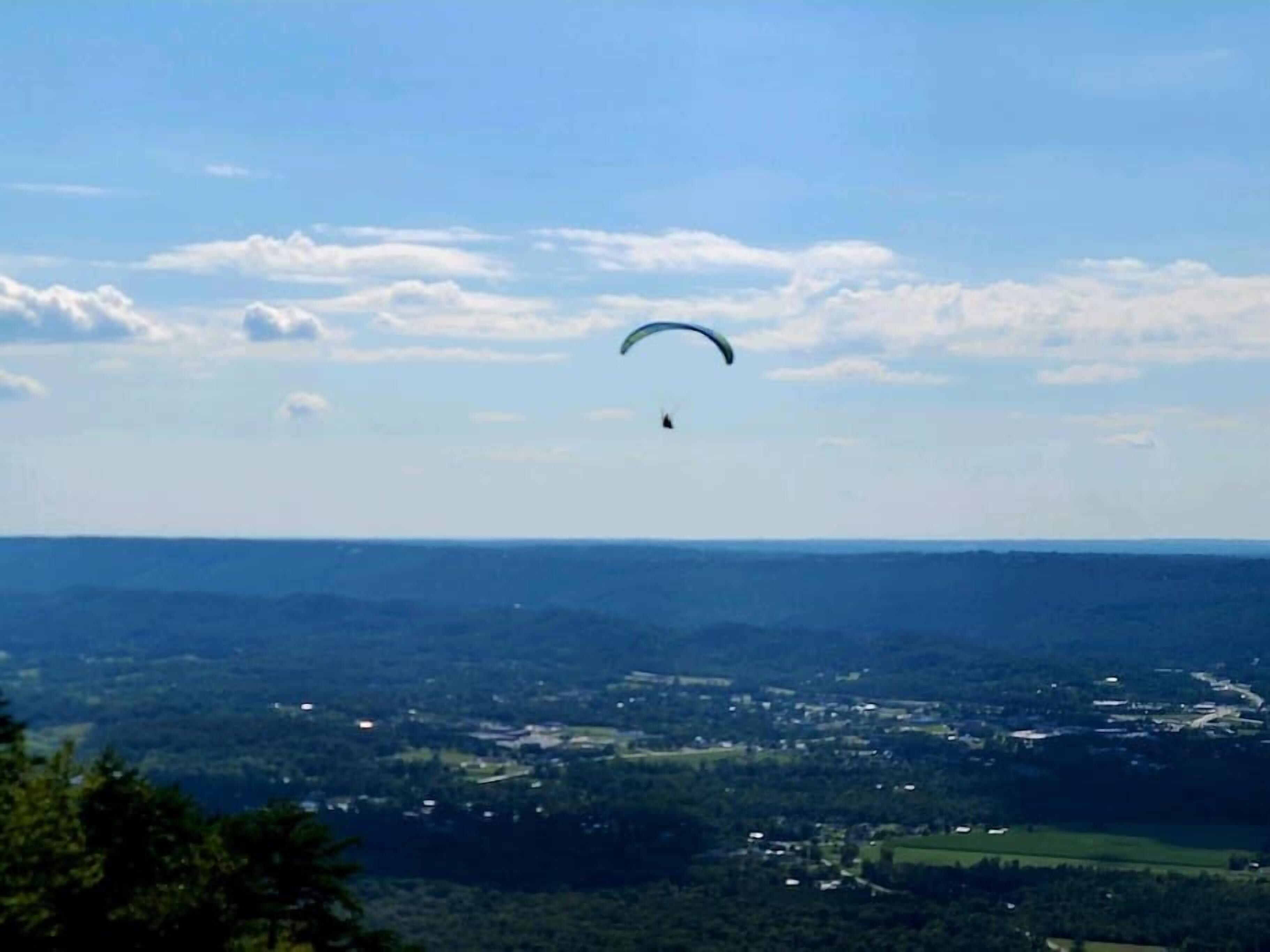 A person paragliding over a landscape with a clear sky and distant buildings.