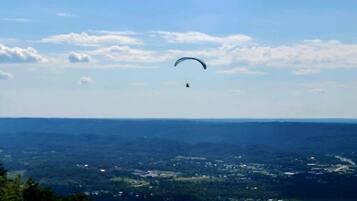 A person paragliding over a landscape with a clear sky and distant buildings.