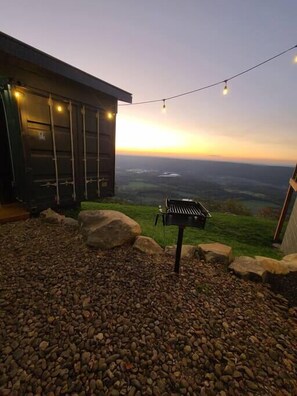 Eine Terrasse im Freien mit Grill, Lichterkette und Blick auf die Landschaft.