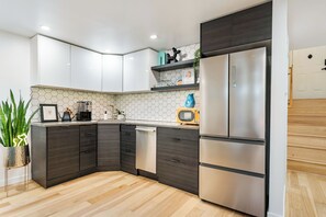Une cuisine moderne avec des meubles de couleur sombre, un réfrigérateur en acier inoxydable, un four à micro-ondes et une machine à café.