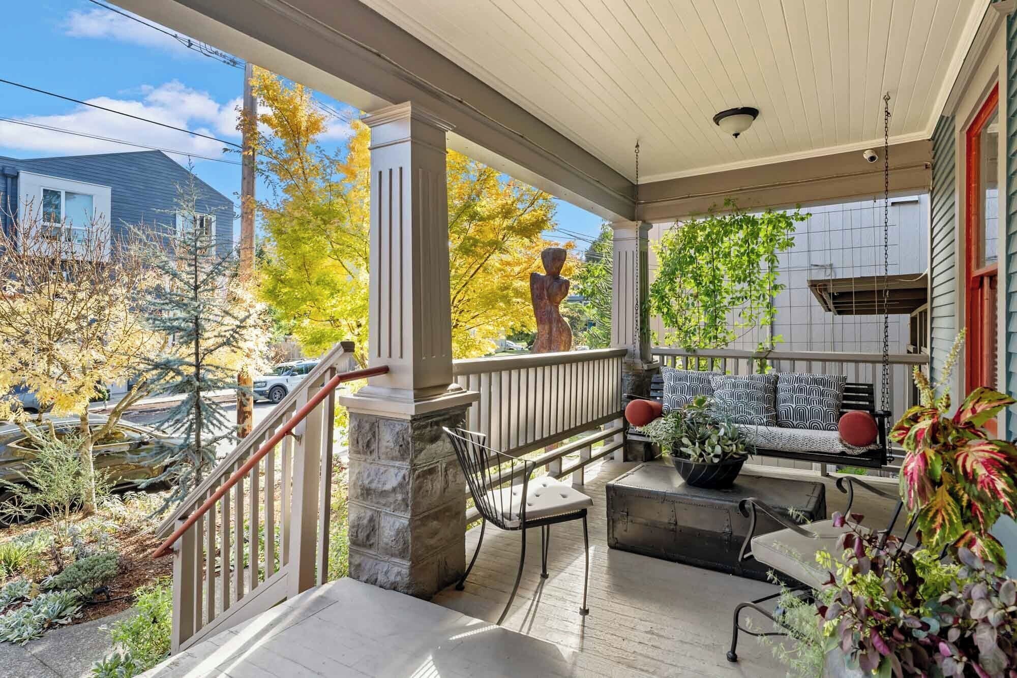 A covered porch with a stone column, outdoor seating, and a statue.