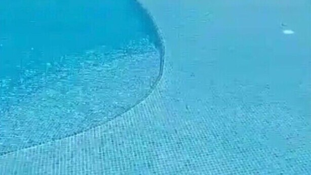 Ein klares, blaues Schwimmbecken mit Liegestühlen und ein Gebäude mit rotem Dach im Hintergrund.