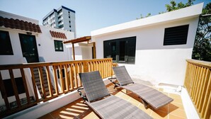 A rooftop terrace with two sun loungers, a wooden railing, and a view of a building with a tiled roof and a door marked with the number 8. - CS5- Preserved Colonial 1BR with High Ceilings- Sleeps 4 (San Juan)