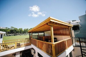 A wooden deck with a railing, a covered seating area, and a view of a green field.