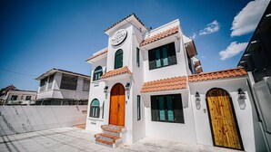 A two-story building with a white facade, a red-tiled roof, and a wooden door. - CS5- Preserved Colonial 1BR with High Ceilings- Sleeps 4 (San Juan)