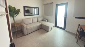 A modern living room with a beige sectional sofa, a potted plant, a small table, and a door leading outside. - CS5- Preserved Colonial 1BR with High Ceilings- Sleeps 4 (San Juan)