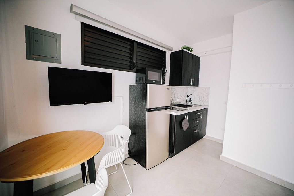 A compact kitchen with a built-in microwave, a refrigerator, and a small countertop. There is a wooden table and two white chairs.