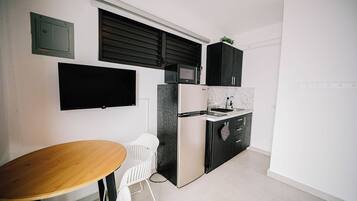 A compact kitchen with a built-in microwave, a refrigerator, and a small countertop. There is a wooden table and two white chairs.