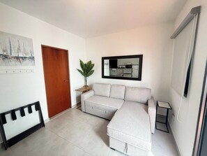 A modern living room with a sectional sofa, a wooden door, a potted plant, and a framed picture on the wall.