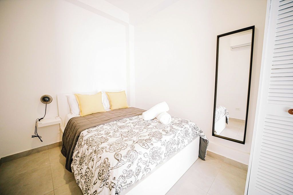 A bedroom with a bed, bedside lamps, a mirror, and a white wardrobe.