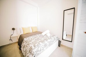 A bedroom with a bed, bedside lamps, a mirror, and a white wardrobe.