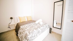 A bedroom with a bed, a bedside lamp, a mirror, and a window. - CS5- Preserved Colonial 1BR with High Ceilings- Sleeps 4 (San Juan)