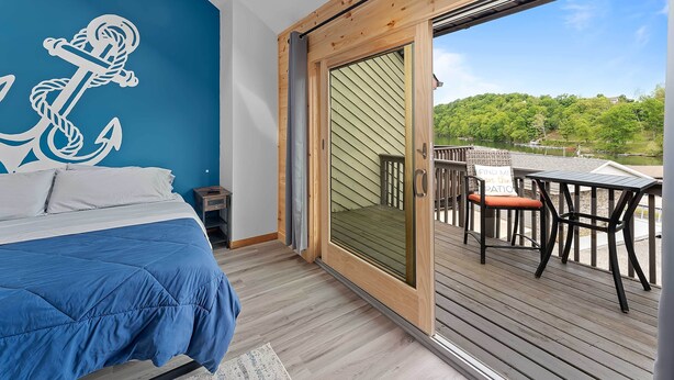 A bedroom with a bed, a large window, and a view of a deck.