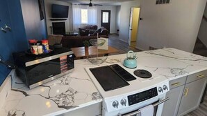 A compact kitchen with a built-in stove, oven, and microwave. There is a dining area with a couch and a TV in the background.