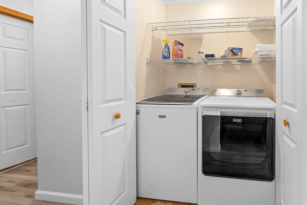 Une buanderie équipée d’un lave-linge, d’un sèche-linge et d’étagères où sont rangés les produits de nettoyage.