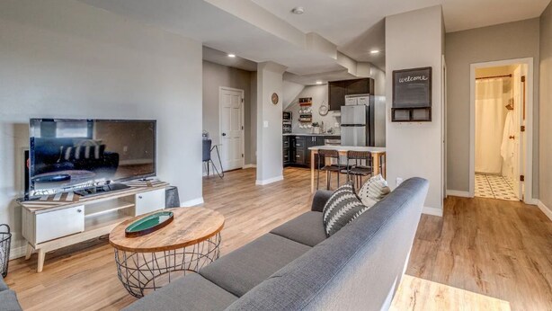 A modern living room with a flat-screen TV, a sofa, a coffee table, and a dining area with a table and chairs.