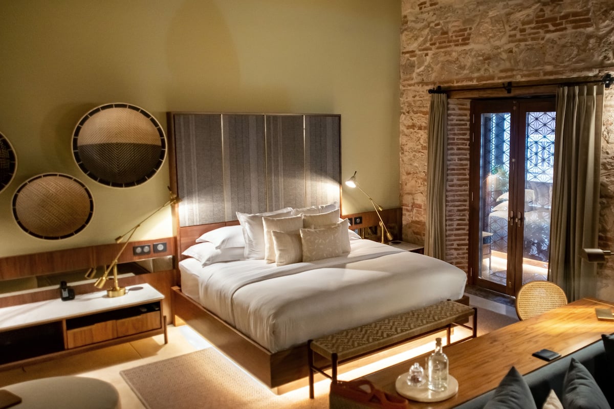 A hotel room with a large bed, bedside lamps, a wooden nightstand, a small table, and a view of the outdoors through a glass door.