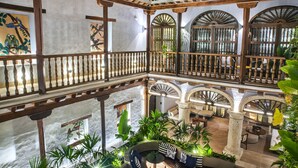 A multi-level atrium with wooden railings, stone columns, and lush greenery. - Hotel Boutique Casona del Porvenir (Cartagena)