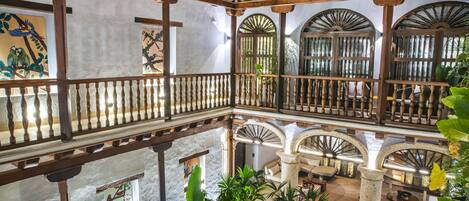 A multi-level atrium with wooden railings, stone columns, and lush greenery.