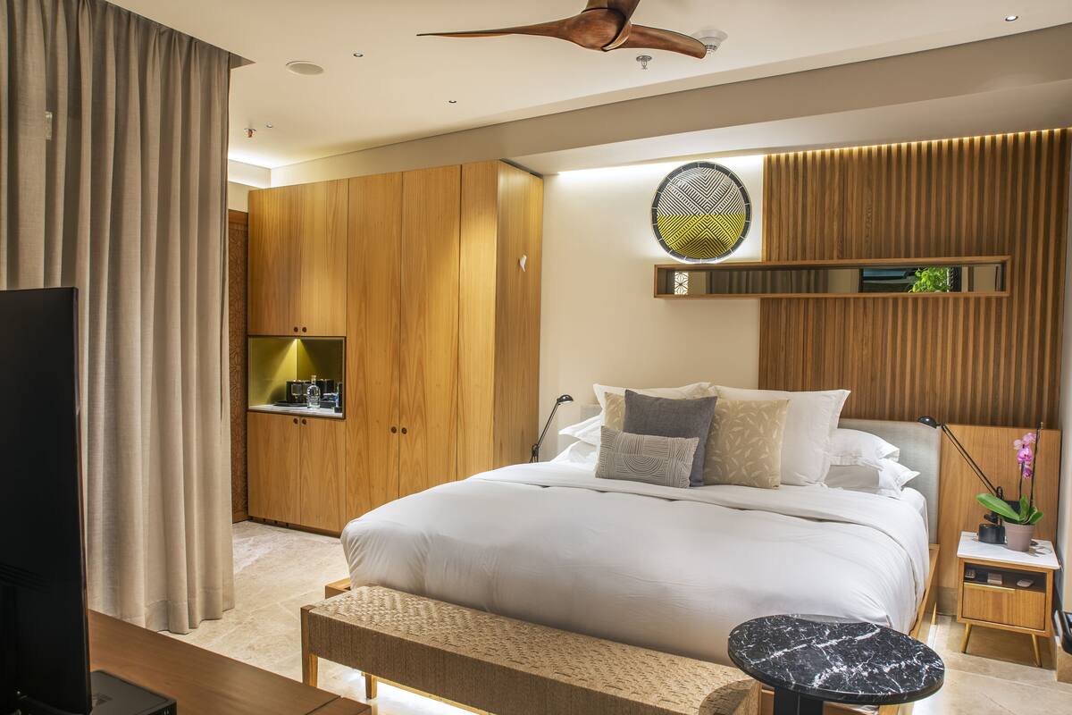 A modern bedroom with a large bed, wooden wardrobe, and a small bedside table with a lamp and plant.