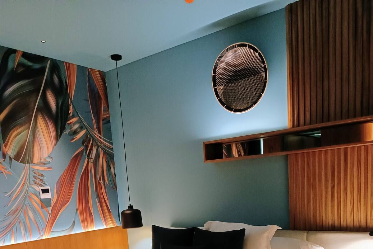 A modern bedroom with a large bed, a wall mural, a round woven light fixture, and a wooden headboard.