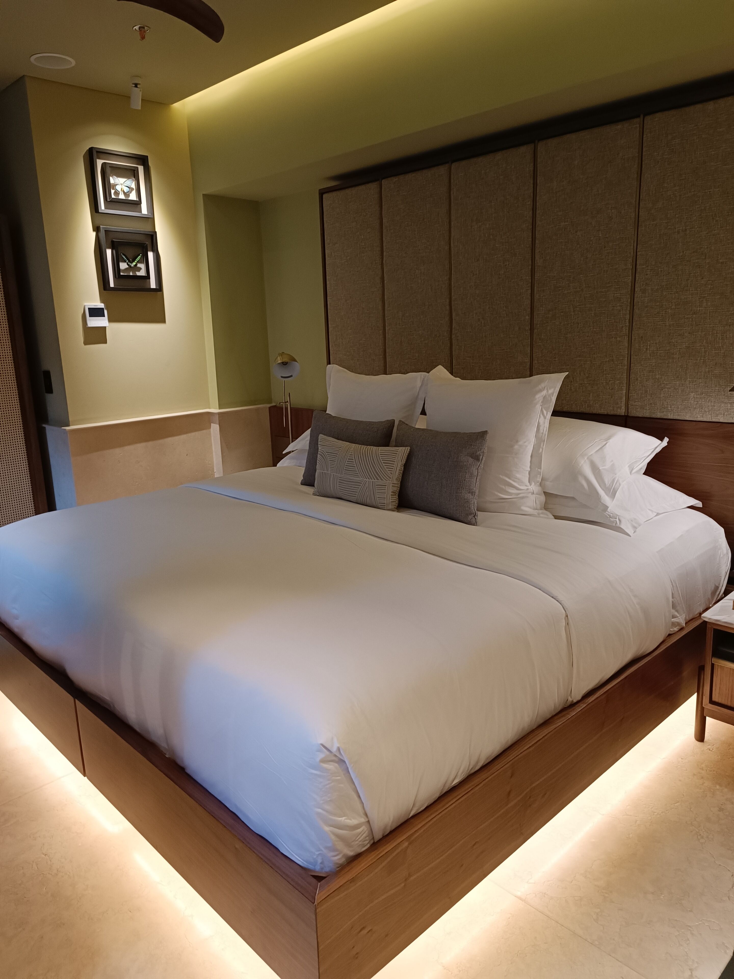 A modern hotel room with a large bed, wooden headboard, and a bedside table.
