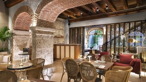A restaurant with brick arches, wooden beams, wicker furniture, and a view through a large window.