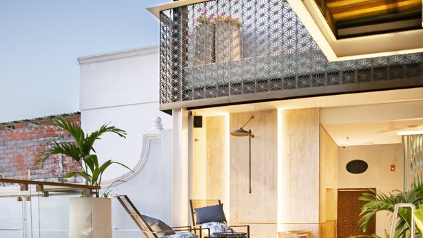 A modern outdoor pool area with a lounge chair and a small table, surrounded by a geometric patterned fence.