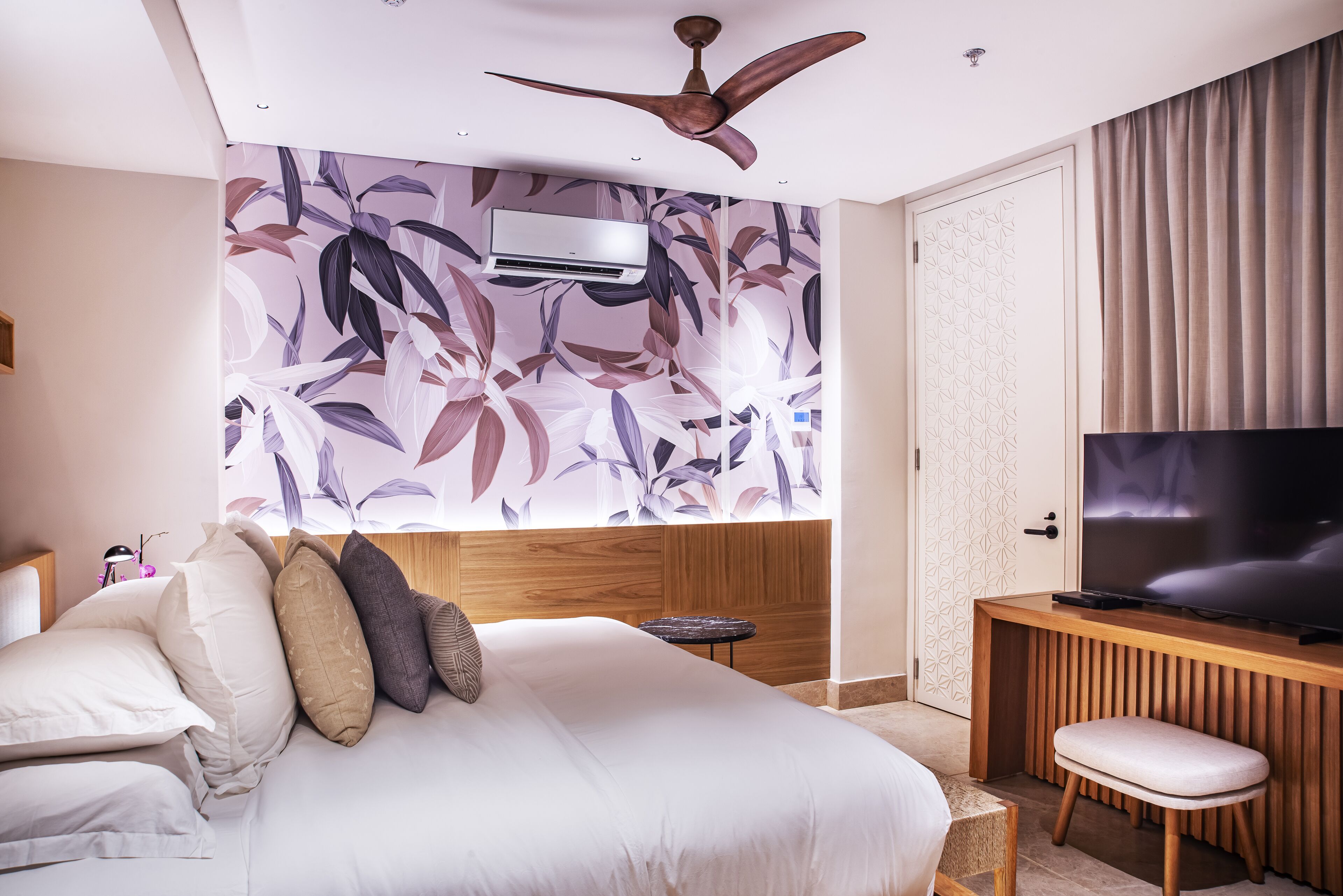 A modern hotel room with a large bed, a ceiling fan, a flat-screen TV, and a wooden desk.