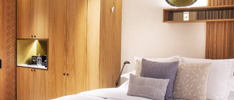 Un dormitorio con un armario de madera, una cama con varias almohadas, una mesita de noche con lámpara y un espejo de pared.
