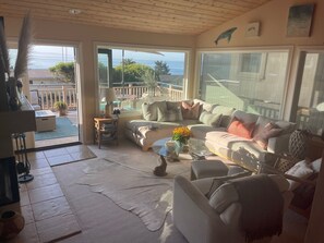 A cozy living room with a large window overlooking a balcony, a sofa, a coffee table, and a lamp. - Lovely Shell Beach home boasts stunning ocean and mountain views- monthly rental (Pismo Beach)