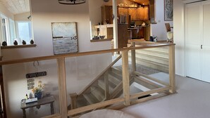 Un interior espaiós amb una escala de fusta, una cuina amb armaris de fusta i una zona de menjador amb taula i cadires.