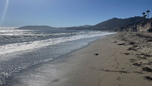 Una platja amb onades, cel blau i muntanyes allunyades.