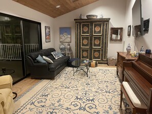 Un salon avec un canapé en cuir noir, une table basse en verre, un tapis à motifs, un meuble en bois et un piano.