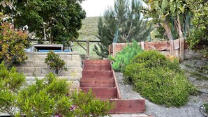 Jardí amb escales de fusta, diferents plantes i una paret de pedra.