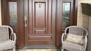 Una porta d'entrada de fusta amb un tirador de bronze, flanquejada per dues cadires de vimetla amb coixins.